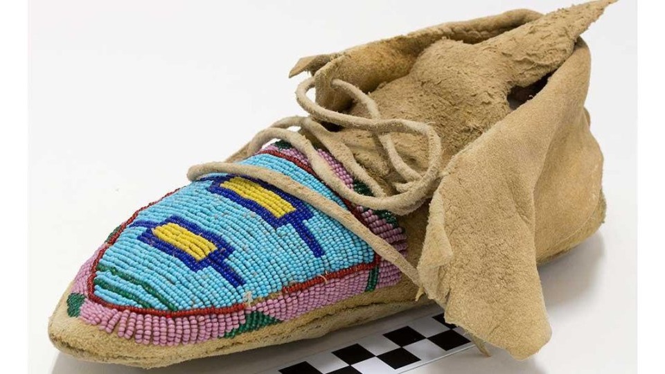 Hide with pink, green, blue, and yellow geometric beadwork on vamp and blue, white, red, and green geometric beadwork along outside side. Added hide cuff, soft hide sole, and triangular hide tongue. Hide thong tie closure threaded through holes cut in cuff corners.