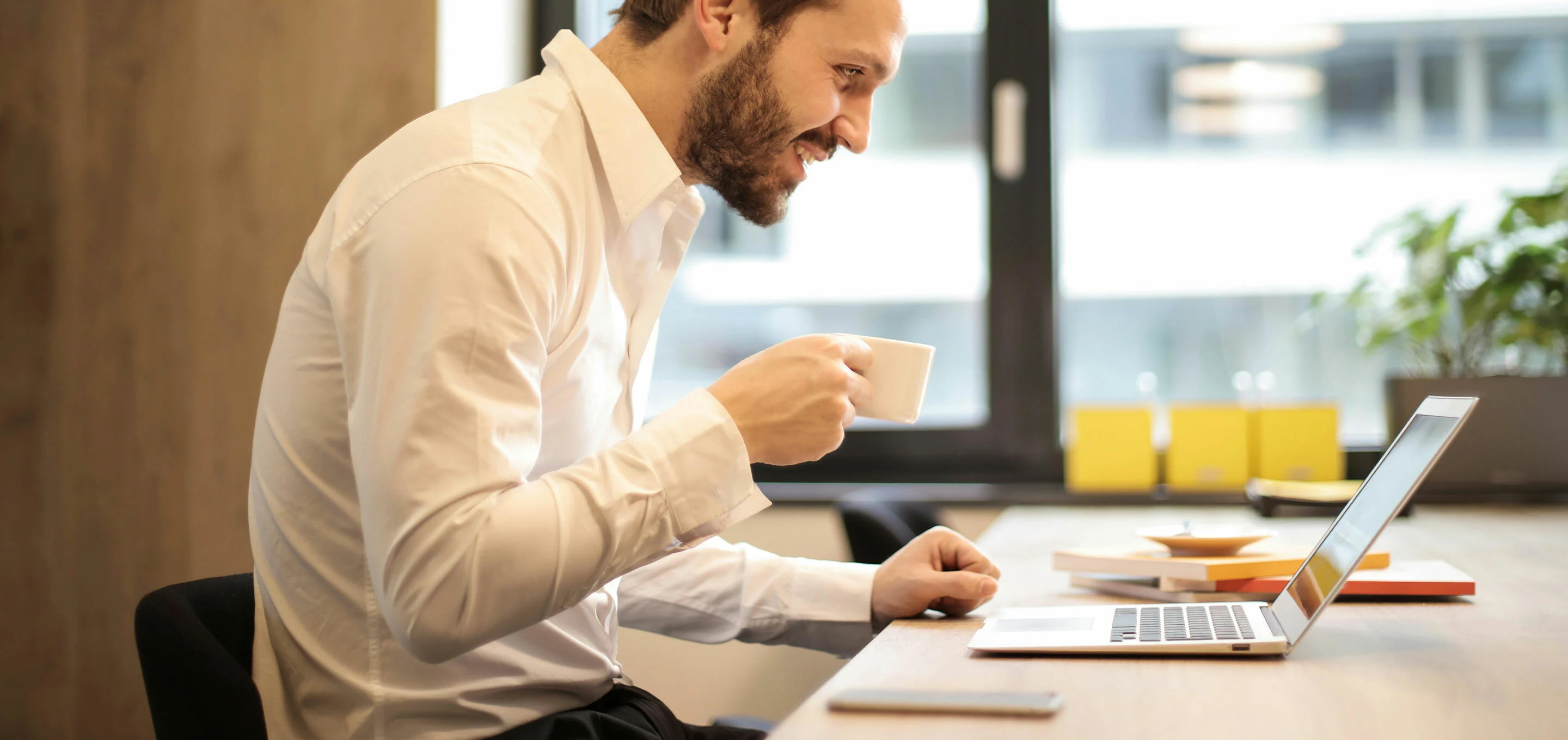 Glücklicher Mitarbeiter im Büro mit Espressotasse schaut auf Bildschirm