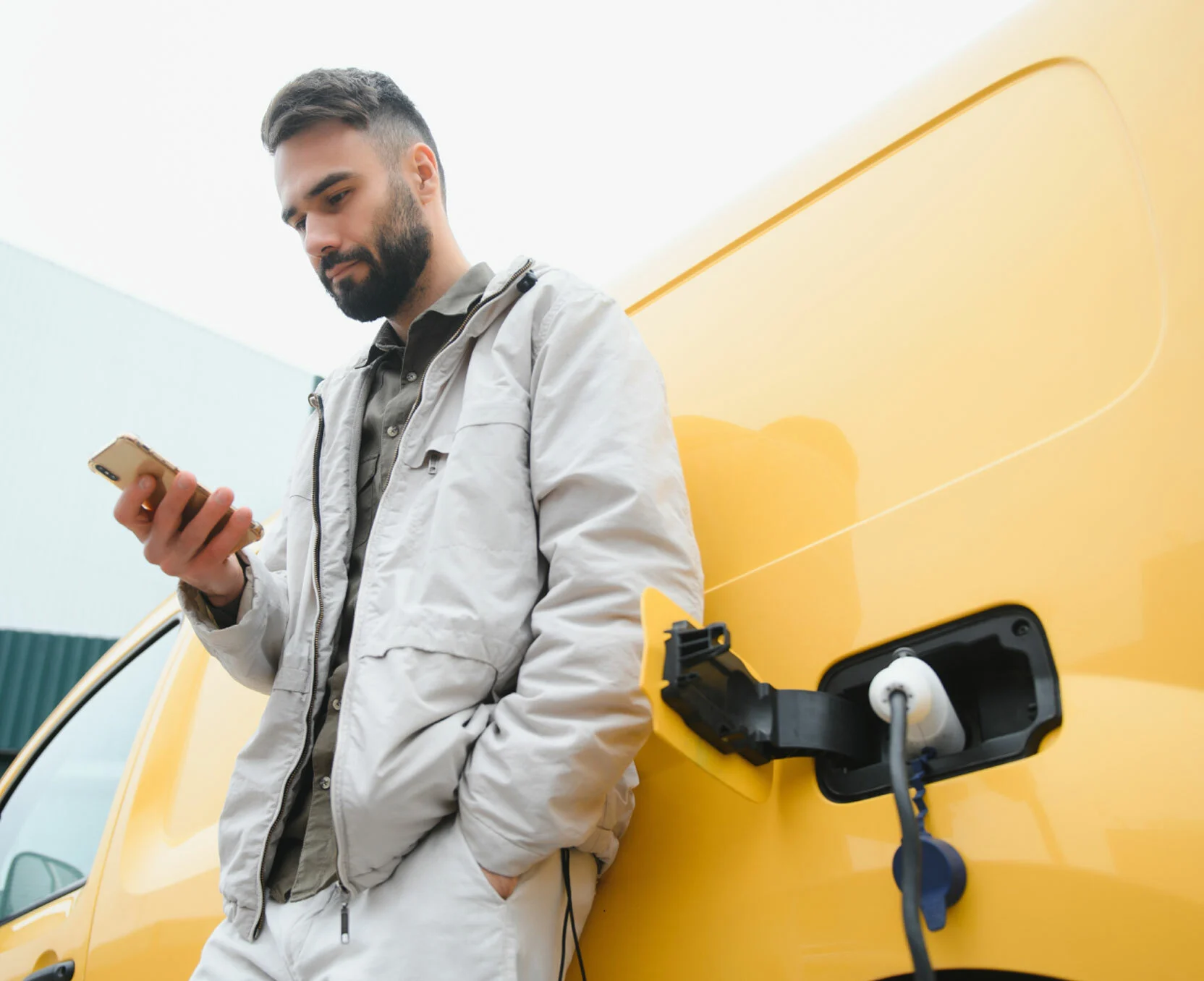 Mann lehnt sich an ein gelbes Elektrofahrzeug und nutzt sein Smartphone, während das Fahrzeug geladen wird.