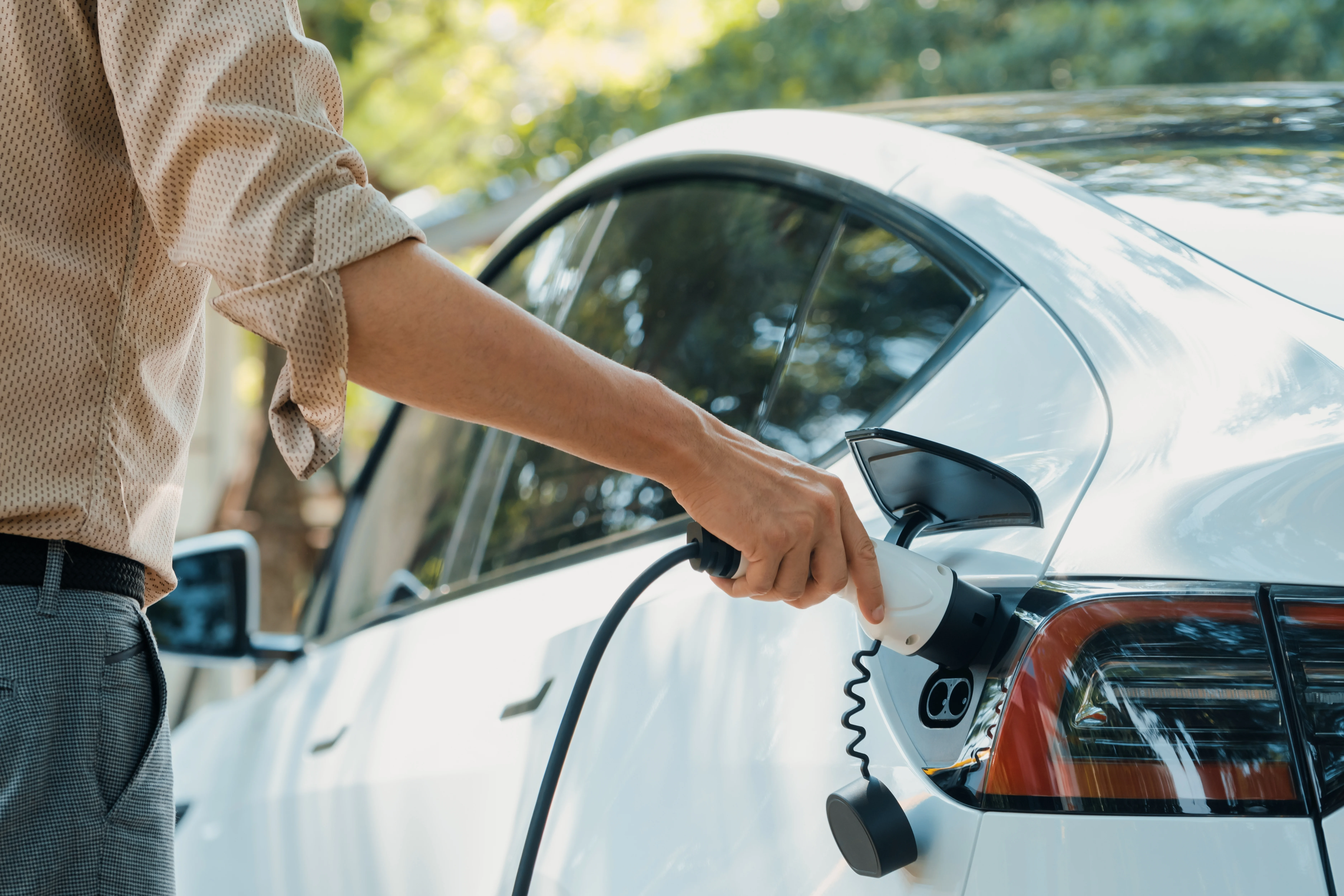 Person steckt ein Ladekabel in ein Elektroauto