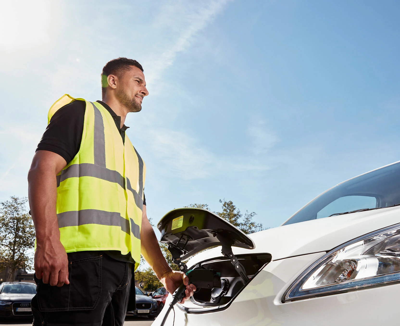Un homme en gilet de sécurité recharge sa voiture électrique.