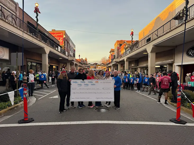 People stand in the middle a crowded downtown street holding a check presented by Clayton to the Morristown Regional Cancer Center for $67,334