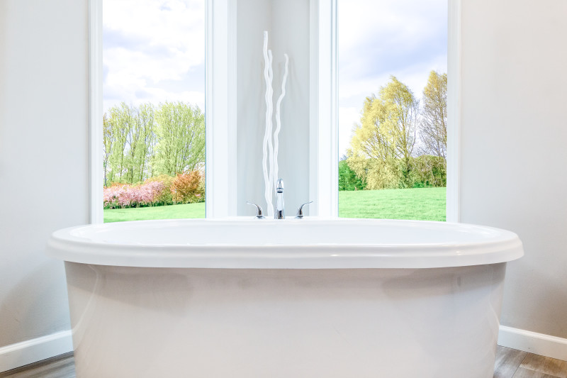 Large white soaker tub in front of a white wall with two large window features.