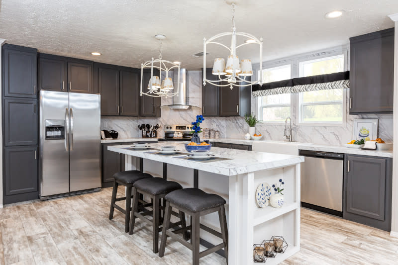 A kitchen in a manufactured home with a white kitchen island with stools and gray cabinets.