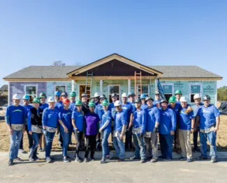 Clayton team members in blue shirts and hard hats stand in front of a home they're building.