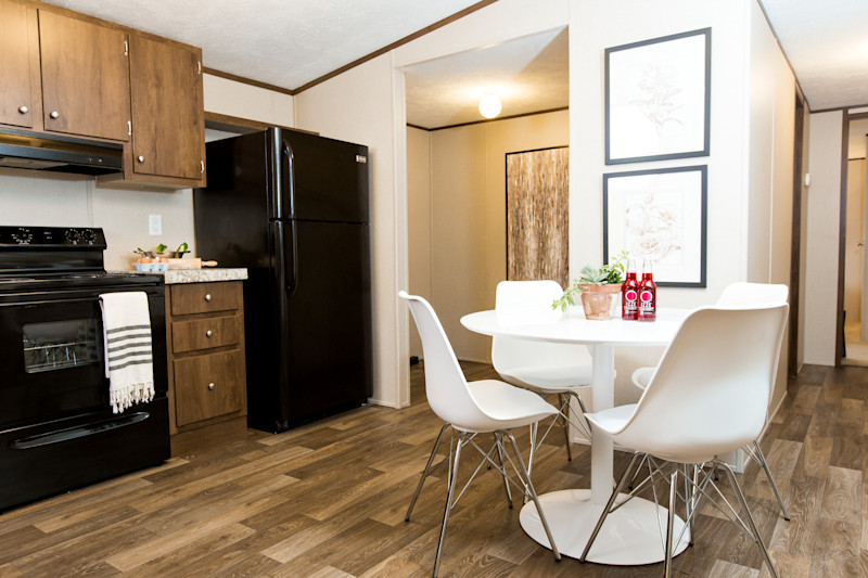 Kitchen of a Clayton manufactured home with dark wood cabinets, black appliances and a table and chairs.