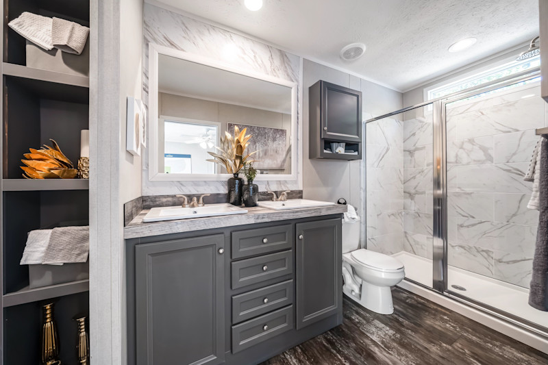 Bathroom of a Clayton manufactured home with built-in cubbies, a vanity, storage over the toilet and shower with a window above it.