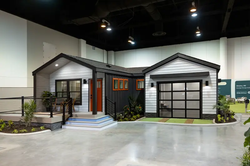 A CrossMod manufactured home inside of a convention center, with black and gray siding.