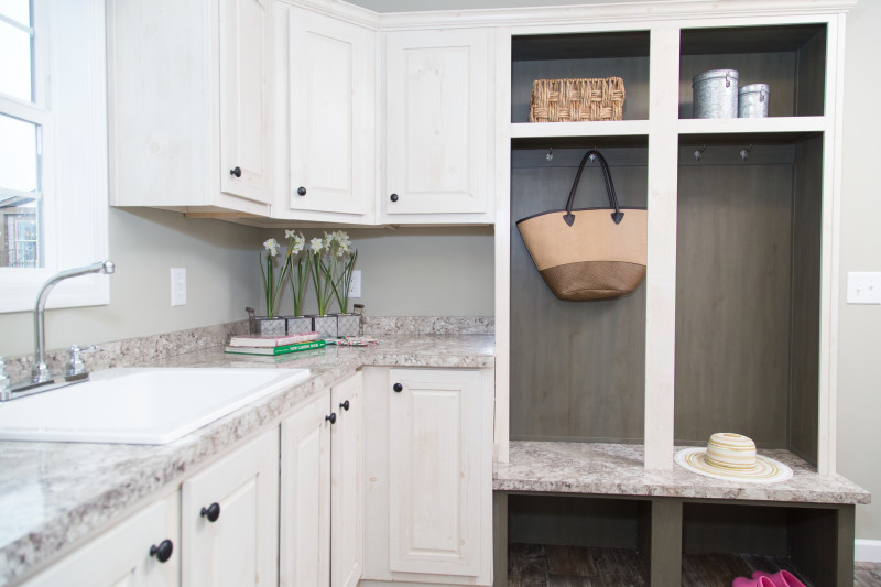 View is of a utility room with white cabinets, a sink, and a built-in hall tree with accessories in it.