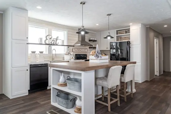 The [model name] features a beautiful kitchen with an island with storage shelves and a shiplap backsplash.
