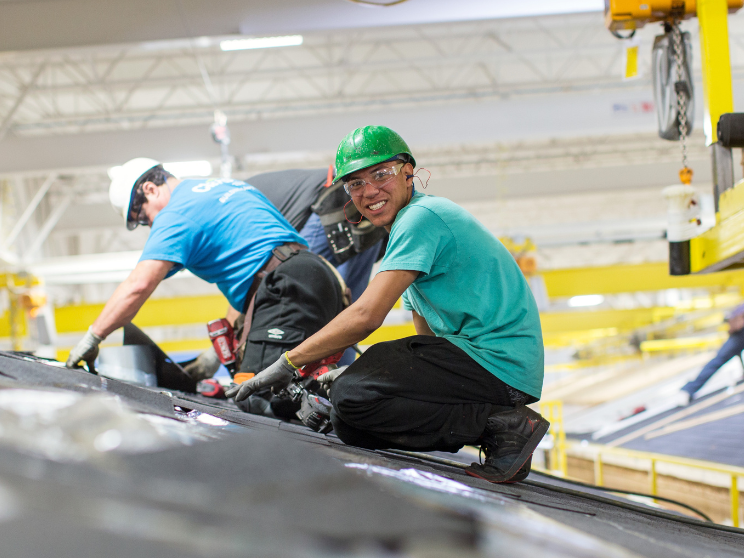 Three men work on a manufactured home's roof in a building facility.