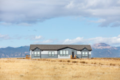 Exterior of a manufactured home with blue and white siding, with yellow grass and blue sky and mountains in the background