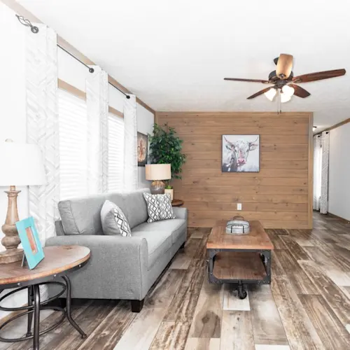 This living room is bright and open, with wood trim, a ceiling fan, wood accent wall and rustic wood-style flooring.