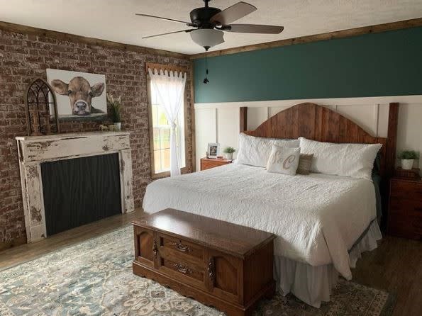 Primary bedroom with green accent wall, white bed, brick accent wall and fireplace.