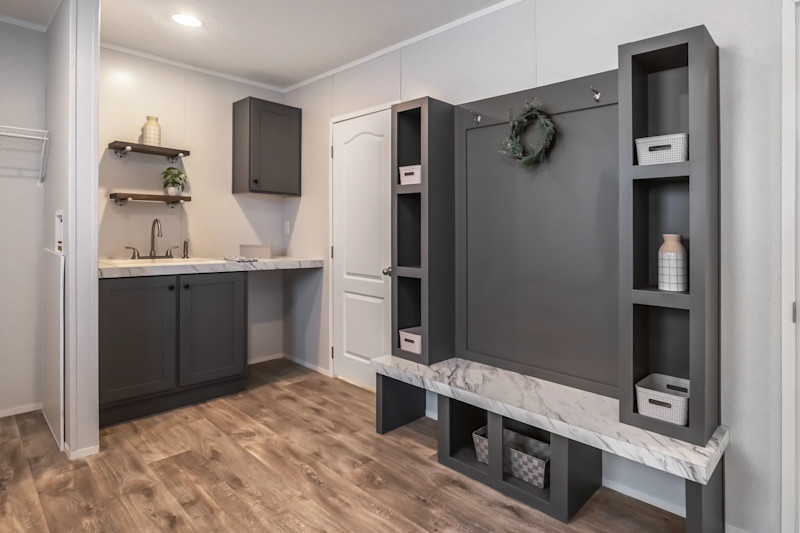 Utility room of a Clayton home with a built-in bench with cubbies and a wall with shelves, with a sink and storage in the background.