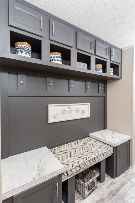 A mudroom in a manufactured home with five coat hooks, cabinets, storage cubbies and a built-in bench.
