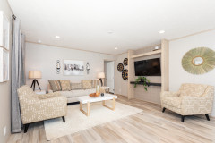 A bright living room is in view with cream colored furniture, a built in for the flat screen tv, and other monochromatic décor. 