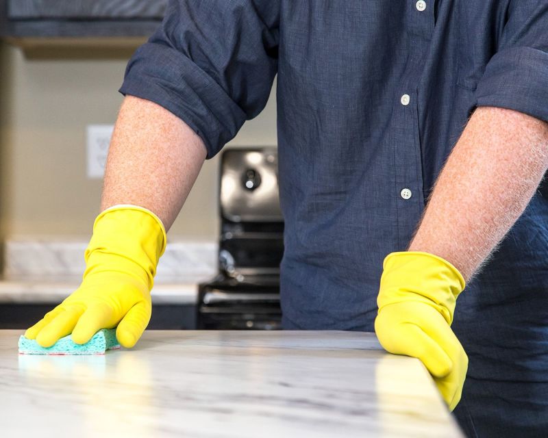 Man with yellow cleaning gloves sponging a counter clean.