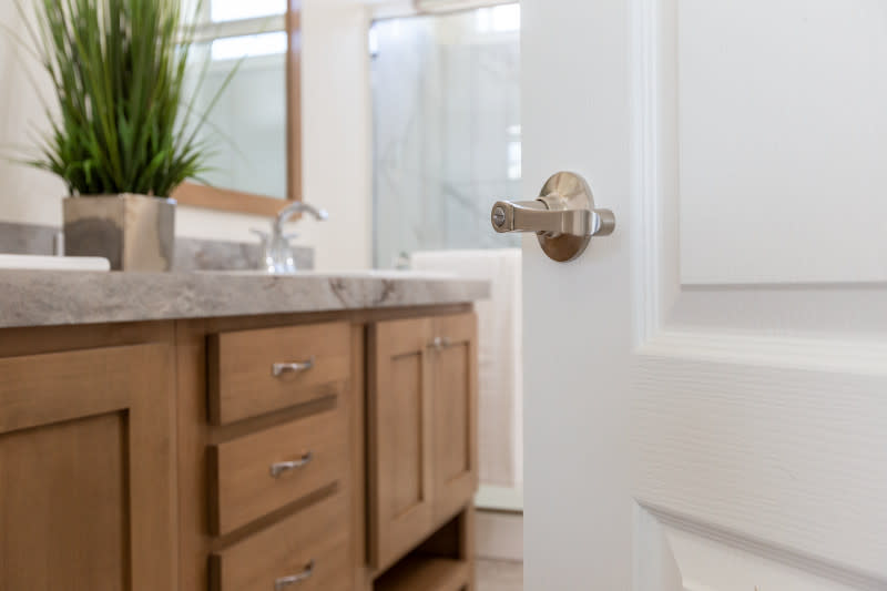 Silver Kwikset door handle in a white door leading into the bathroom of a manufactured home.