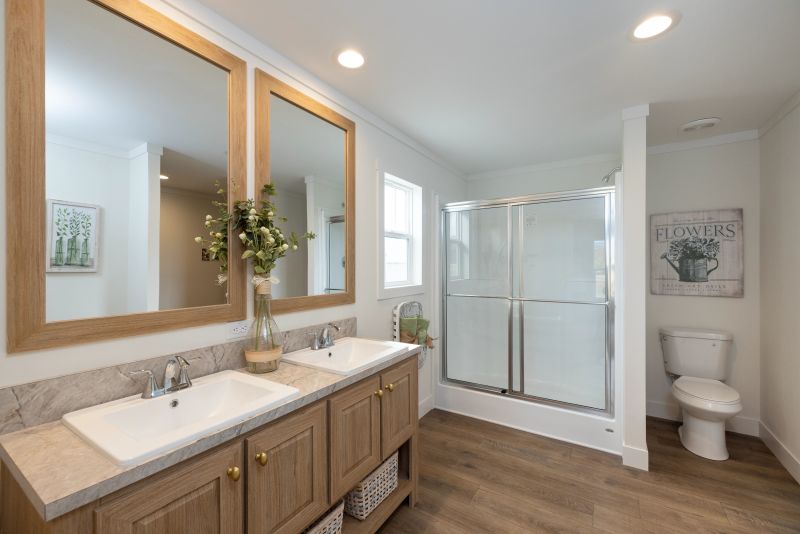 Bathroom with light wooden double vanity and mirrors over them. There's also a walk-in shower and toilet.