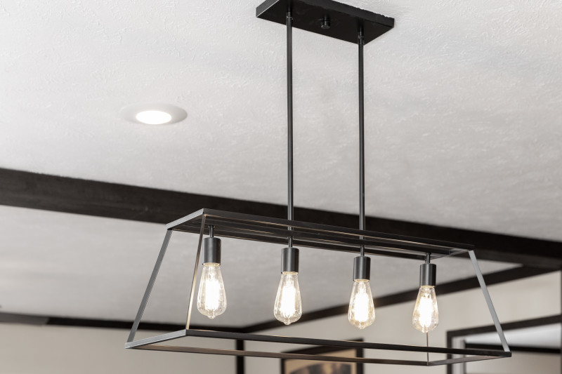 There's a light fixture with black, industrial metal material that creates a see through, outlined shade for 4 individually hanging bulbs.