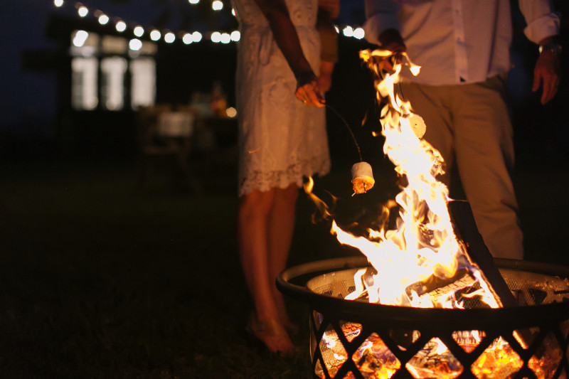 Couple roasting a marshmallow over a fire outside their manufactured home.