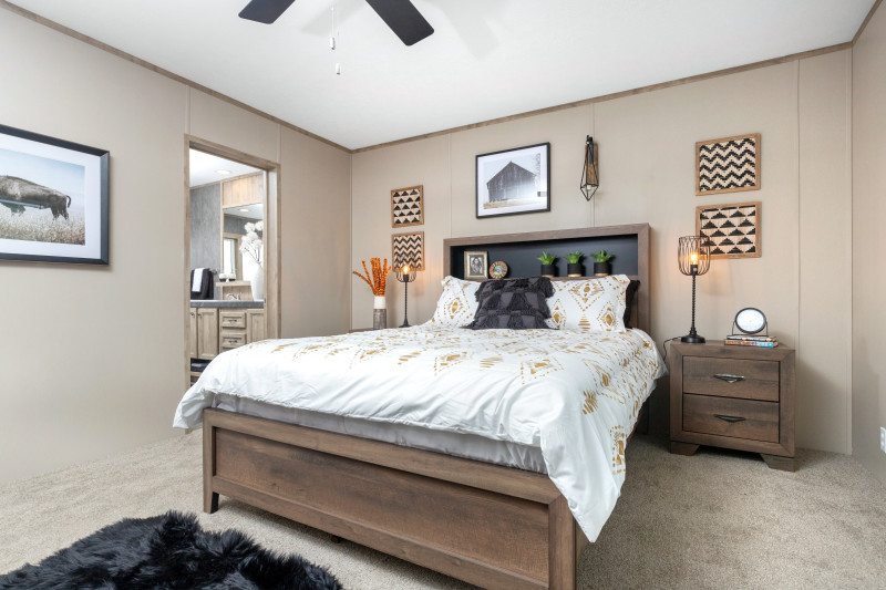 The view of the primary bedroom shows a bed with white bedspread and a wooden bed frame with black headboard. You can see the entry to the attached bathroom off to the side.
