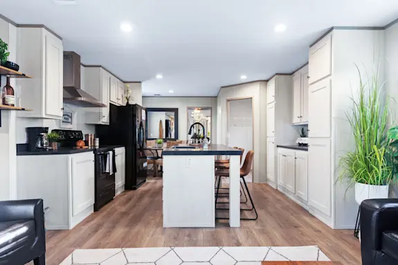The Anniversary 16763S features a large kitchen island with a built-in sink and dark granite-style countertops.
