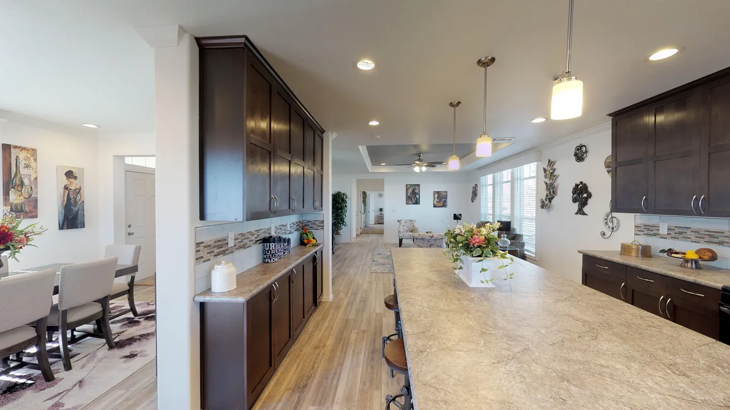 Kitchen of a Clayton manufactured home with an island and rows of dark cabinets on each side, with a dining room off to the left side.