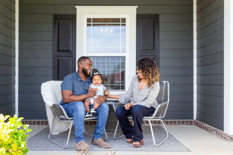 A young couple and their baby sitting on the front porch of their manufactured home.