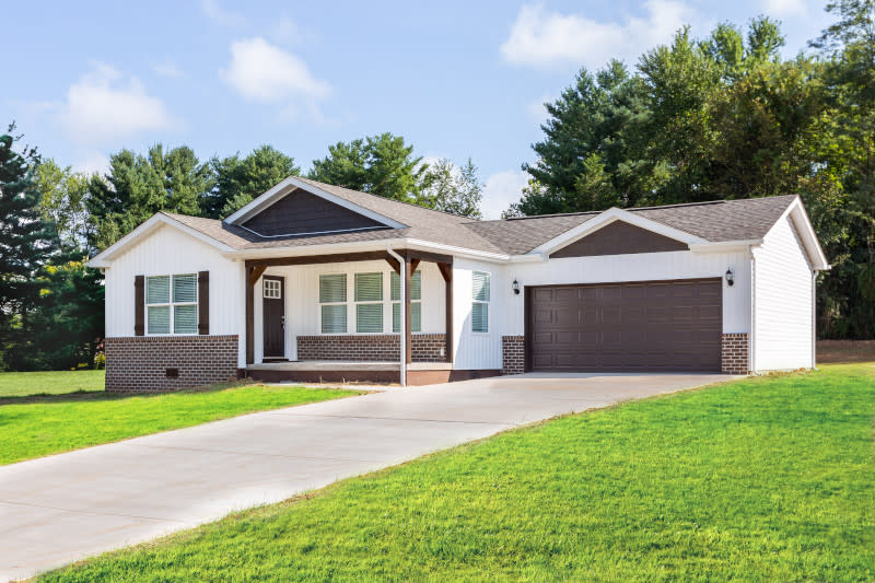 A CrossMod home with white siding, brown brick trim, brown shutters and a brown garage door with a driveway and lawn.