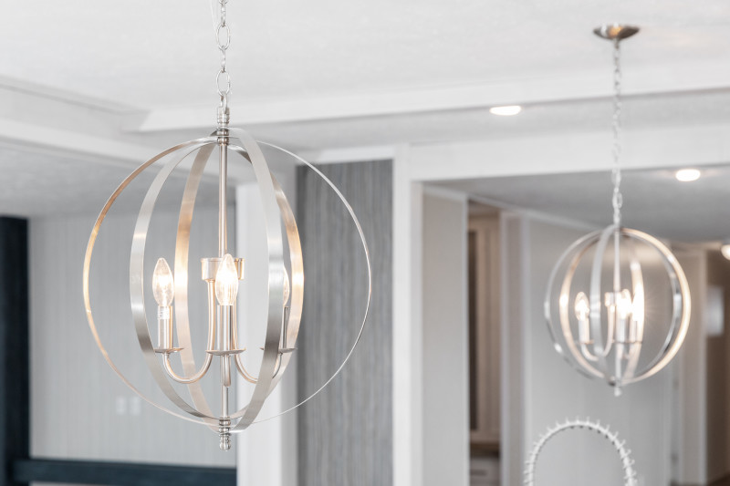 wo modern chandeliers are hanging in a kitchen. The are silver with interlocking circles that make a sphere around the bulbs.