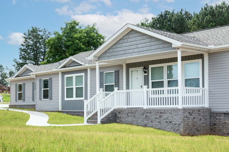The exterior of a manufactured home with an elevated front porch with white railing.
