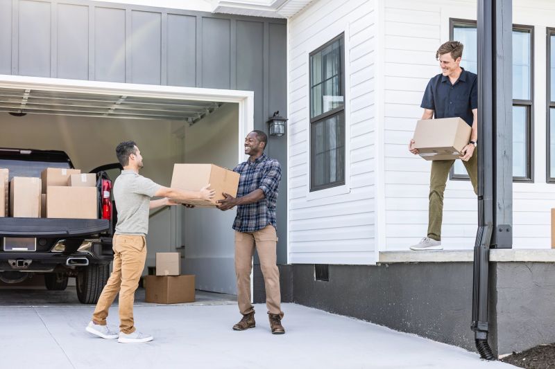 Three friends move boxes from a truck in a garage to the porch of a home