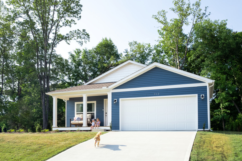 Blue new class Clayton home with golden retriever running down the driveway in front of the white garage door