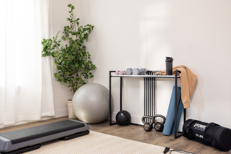 Gym equipment in the flex space of a manufactured him with a table with weights, mats and an exercise ball, and a plant in the corner.