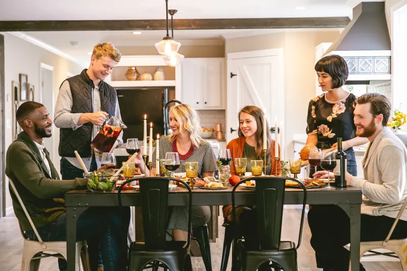 Friends sitting and standing around a Thanksgiving table in their manufactured home kitchen.