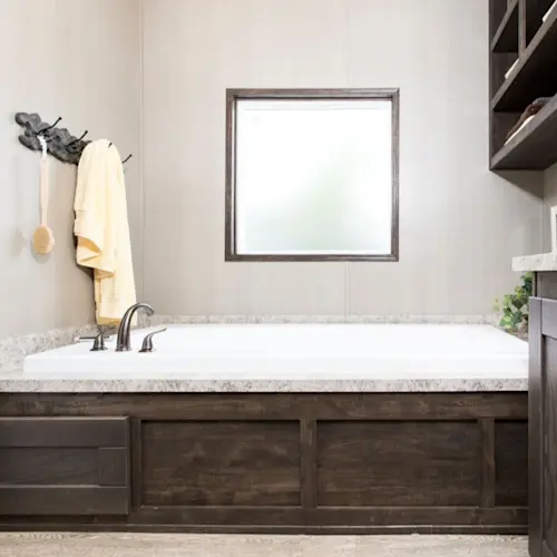 This primary bath found in our Resolution 16763X has a natural look in both design and décor. Complete with wooden cabinets, metallic faucets and a soaking tub, this primary bath is both stylish and functional.