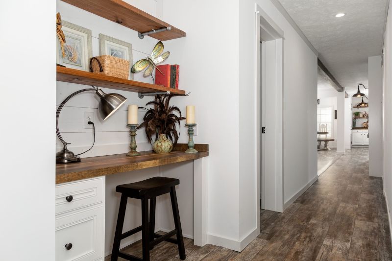 A built-in desk in a hallway, with drawers and three open wooden shelves, with decor and a stool.