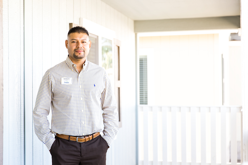 A home center manager in a button up shirt and slacks stands on the porch of a manufactured home.