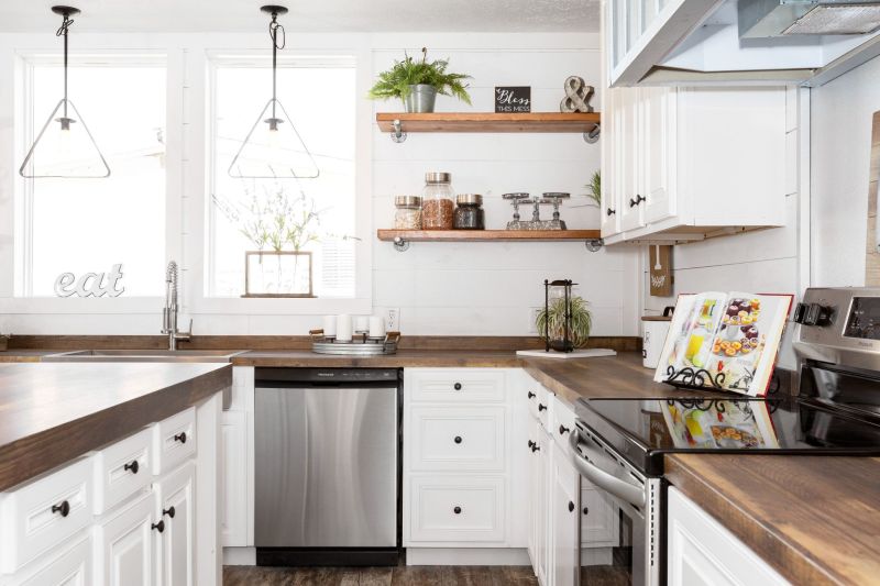 Farmhouse kitchen in a Clayton manufactured home with white cabinets and shiplap walls, stainless steel appliances and farmhouse decor on open shelves.