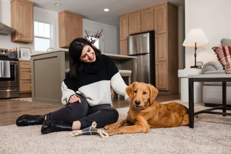 A woman in a sweater sits on the living room floor with her dog.