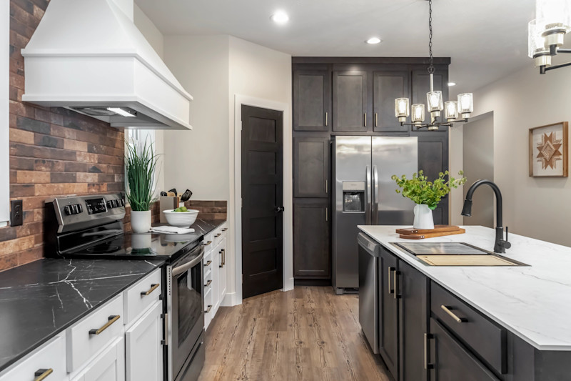 Kitchen of a Clayton manufactured home with an island, stove with range hood and fridge with cabinets around it.