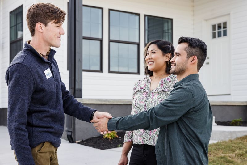 Home consultant shakes hands with a couple outside of a manufactured home