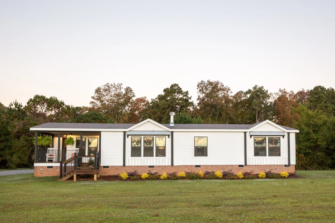  Exterior of a Clayton manufactured farmhouse with white siding and a corner porch. 