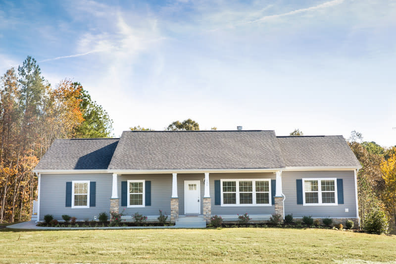 Light blue modular home with a gray roof, white pillars and darker blue shutters.