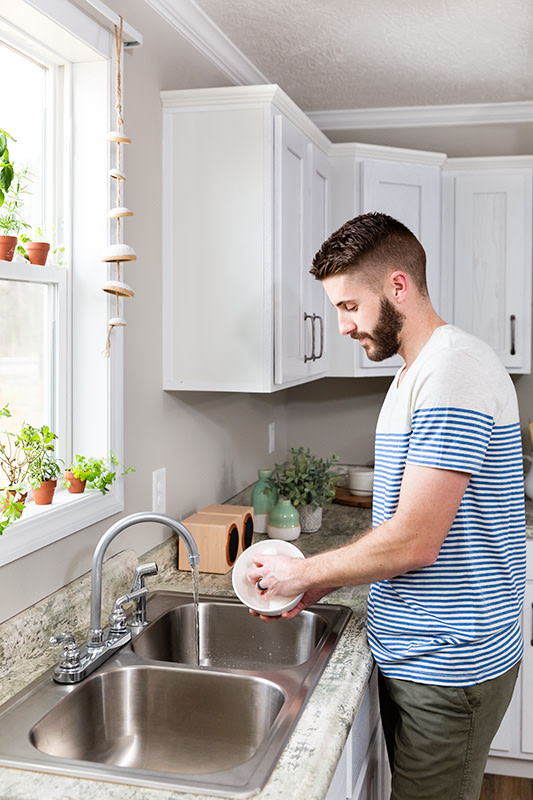 Young man washing a bowl at a kitchen sink in a manufactured home.