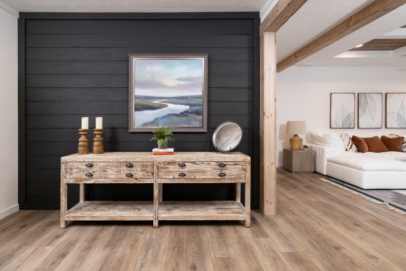 A dark gray entryway wall is seen, decorated with a landscape painting and weathered wood table; part of the living room can be seen from the right side.