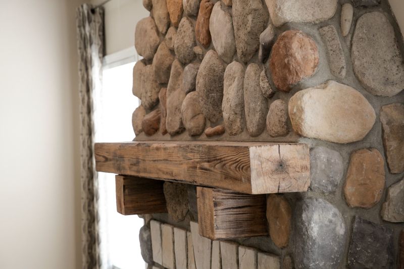 Side view is a close up of a river stone styled fireplace with wooden mantel.