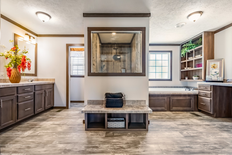 Huge bathroom with shower in the center plus a bench and shower window. A soaker tub is to the right side with a vanity in view. To the left, there are cabinets and double sinks.